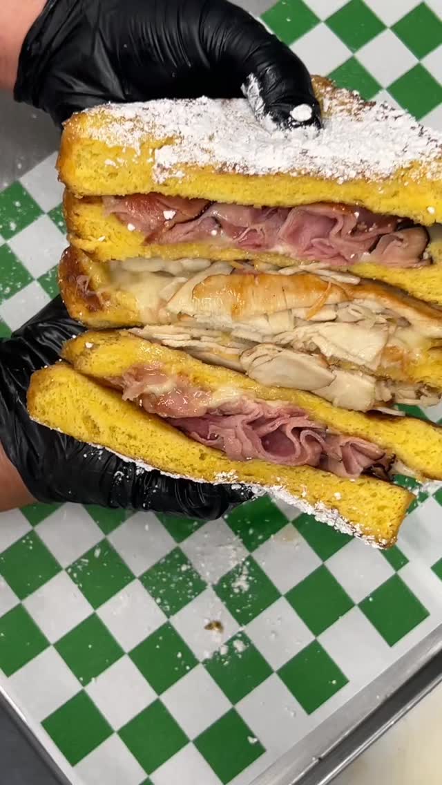 Frisco's Monte Cristo sandwich — golden French toast bread filled with ham and melted cheese, dusted with powdered sugar, served on green-and-white checkered deli paper